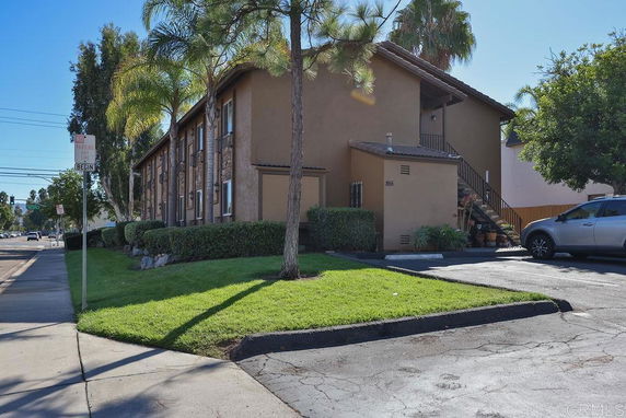 Front view of a two-story apartment building with brown exterior and surrounding greenery.