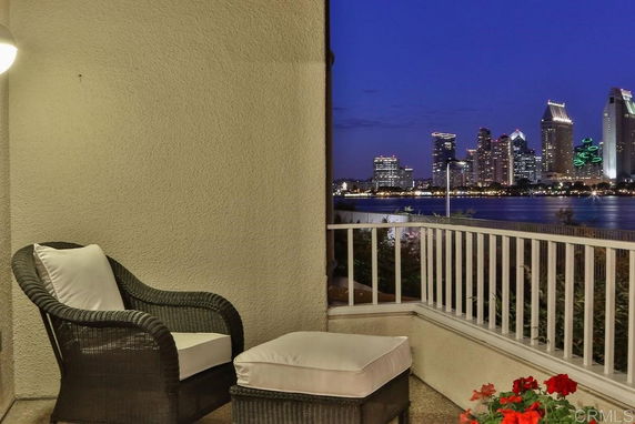 View from a balcony with wicker chair and ottoman overlooking a city skyline at night.