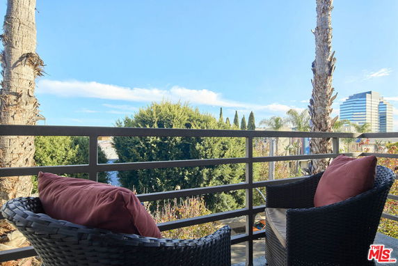 Panoramic view from a balcony with outdoor seating overlooking trees and distant buildings.
