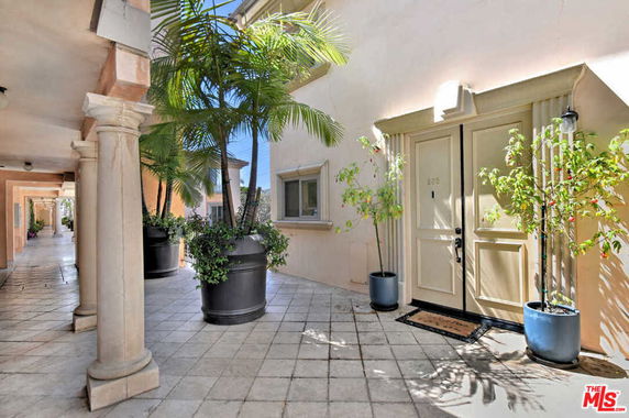 Front view of a building entrance with potted plants on a tiled walkway.