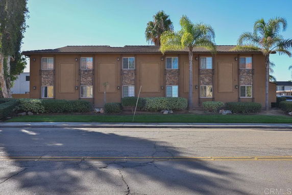 Front view of a two-story building with a brown facade and palm trees nearby.