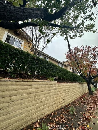 Front view of a multi-story building with a brick retaining wall and surrounding trees.