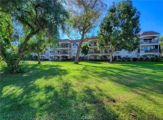 Front view of a multi-story building with balconies and a grassy lawn.
