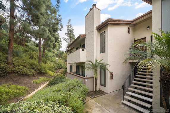 Exterior view of a two-story building with stairs leading to the entrance and surrounded by greenery.