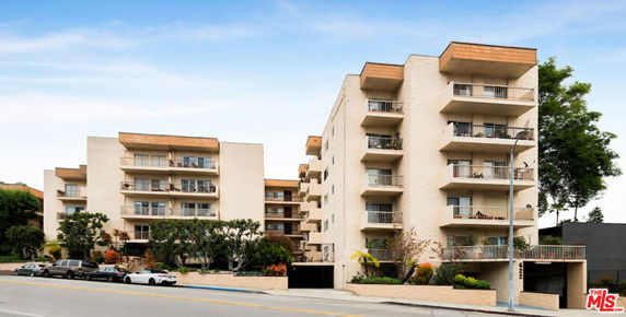 Front view of a multi-story apartment building with balconies and a parking area.