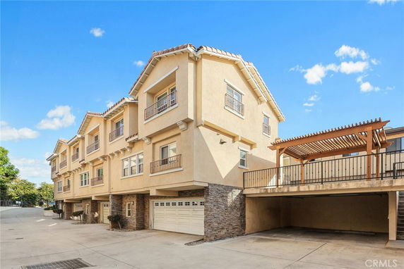 Front view of a multi-story residential building with a parking area and a pergola structure.