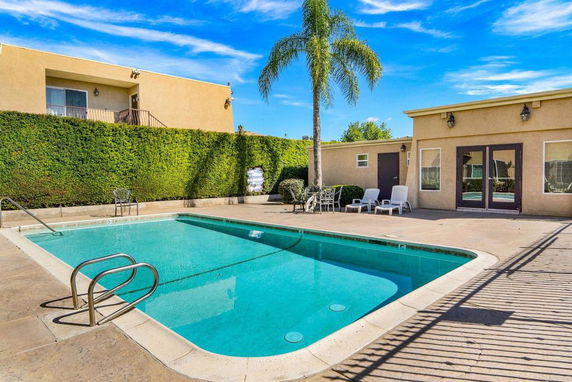 Outdoor swimming pool area with patio seating and a view of adjacent buildings.