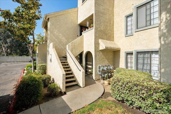 Front view of a multi-story residential building with concrete stairs and bushes.