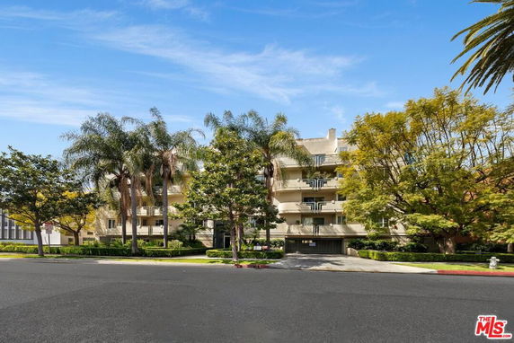 Front view of a multi-story residential building with balconies and surrounding trees.