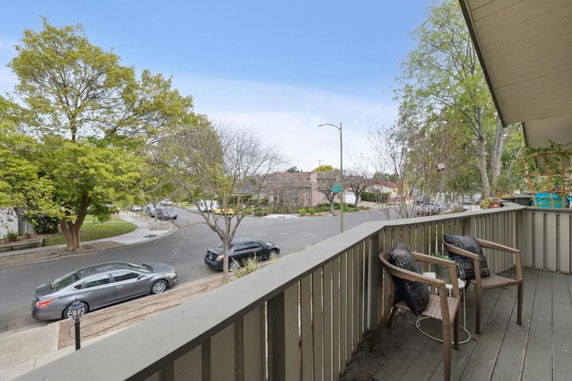 View of a residential street from a balcony with trees and parked cars.
