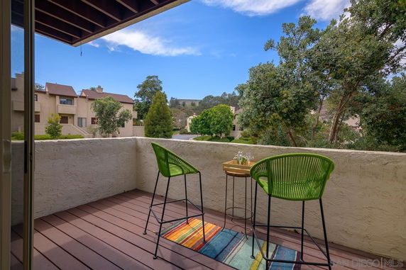 Outdoor balcony with two green chairs and a small table overlooking residential buildings and trees.