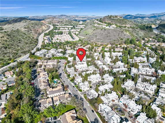 Aerial panoramic view of a residential area with clusters of white buildings surrounded by greenery and hills.
