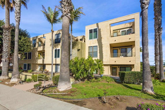Front view of a multi-story apartment building with balconies and surrounding greenery.