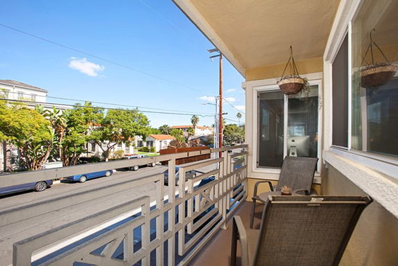 View of a residential street from a balcony with chairs and hanging planters.