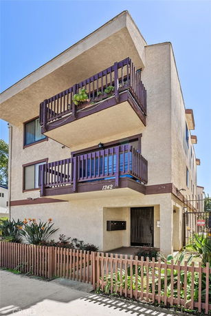 Front view of a three-story building with balconies and a gated entrance.