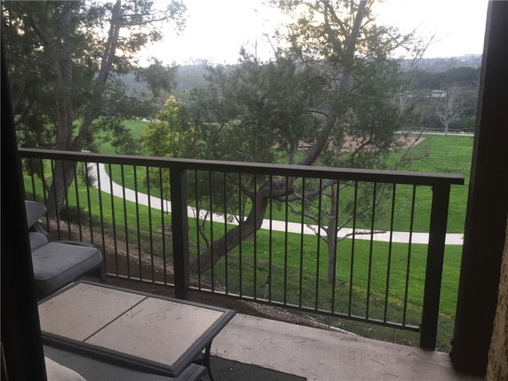 View from a balcony overlooking a green park with winding paths and trees.