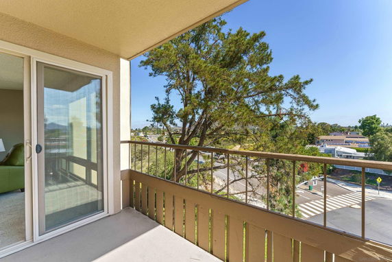 Balcony view overlooking a street with trees and buildings in the background.