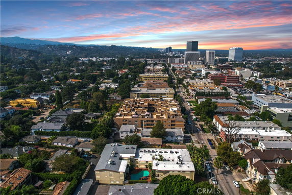 Panoramic view of a cityscape with numerous buildings, roads, and distant mountains under a colorful sky.