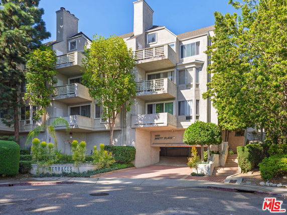 Front view of a multi-story residential building with balconies and trees in front.