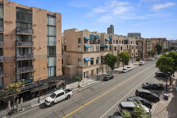 Street view with residential and commercial buildings, parking area, and cars on the road.