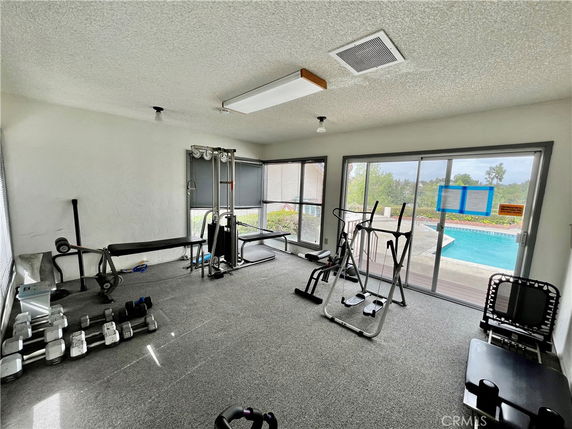 Indoor gym area with exercise equipment and large windows overlooking a swimming pool.