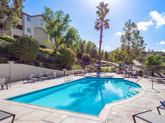 Outdoor swimming pool with lounge chairs and umbrellas, surrounded by trees and shrubs.