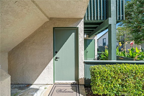 Front view of an entrance with a welcome mat and a green door next to a small garden area.