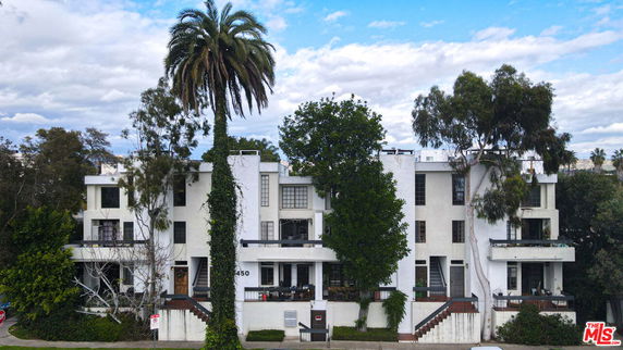 Front view of a multi-story building with balconies and large trees in front.