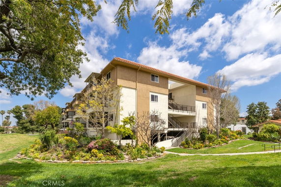 Front view of a multi-story residential building with outdoor stairs and surrounding greenery.