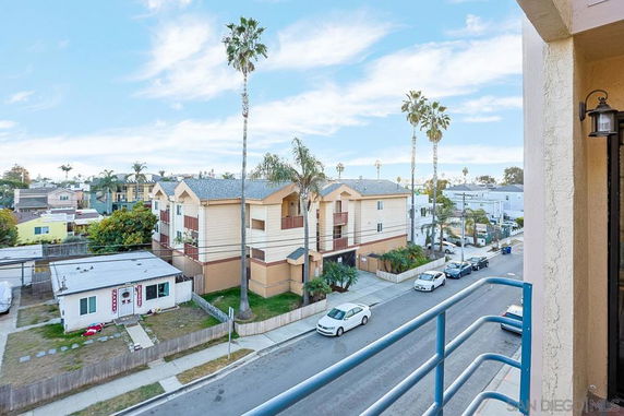 View from a building balcony showing nearby residential buildings and a street with parked cars.
