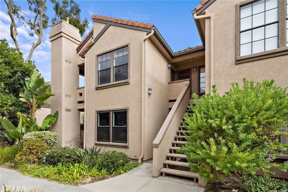 Front view of a beige two-story house with a staircase leading to the entrance and a chimney on the left side.