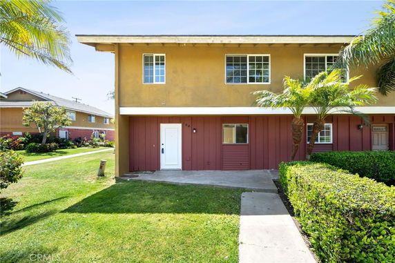 Front view of a two-story house with a small front yard and palm trees.