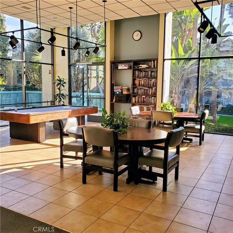 Interior view of a clubhouse with a billiards table, bookshelves, and seating area.