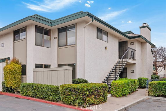Front view of a two-story residential building with external staircase and shrubs.