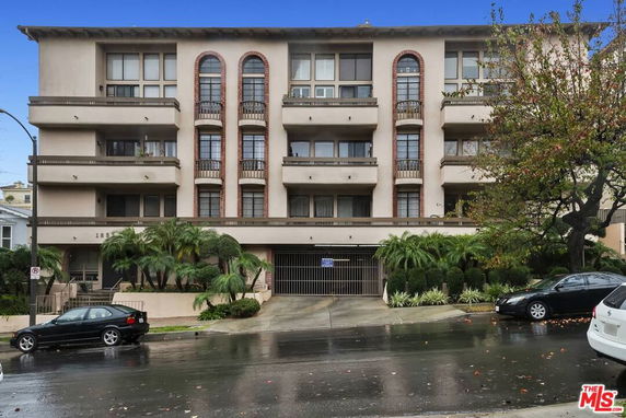 Front view of a multi-story apartment building with balconies and gated entrance.