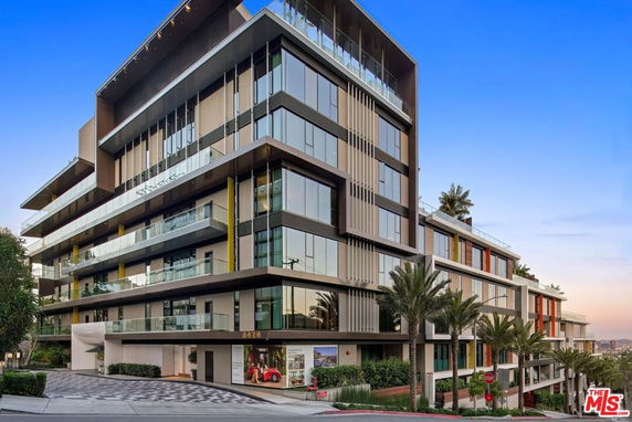 Front view of a modern multi-story apartment building with glass balconies and palm trees around the entrance.