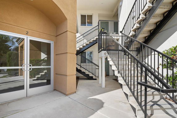 Exterior view of a building with stairs leading to upper levels and glass entry doors.