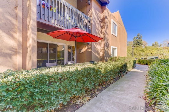 Front view of a multi-story building with a balcony and an outdoor seating area under a red umbrella.