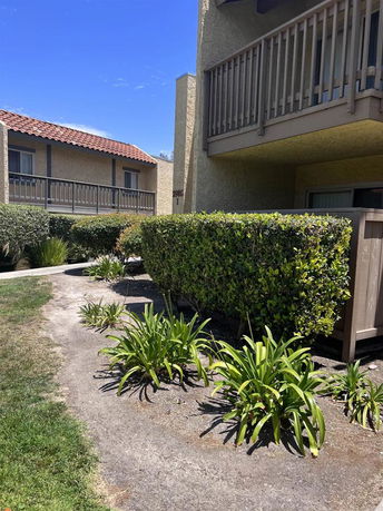 Front view of a two-story apartment building with balconies and shrubs in the foreground.