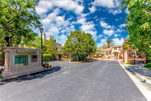 Front view of a gated residential community entrance with a driveway and surrounding greenery.