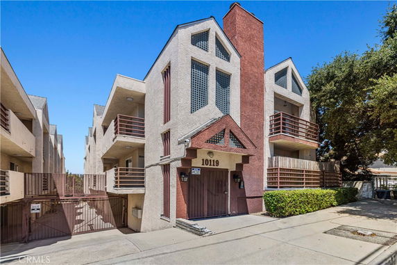 Front view of a multi-story residential building with balconies and a gated entrance.