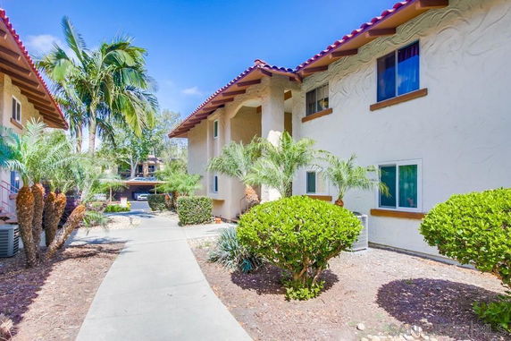 View of a two-story building exterior with a sidewalk and tropical landscaping.