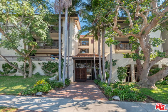 Front view of a multi-story apartment building with balconies and lush landscaping.