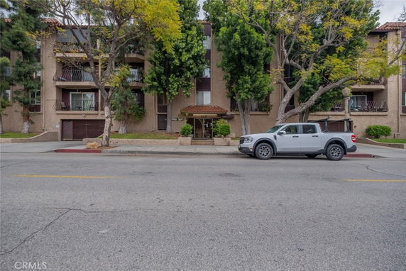 Front view of a multi-story apartment building with balconies and a parking area.