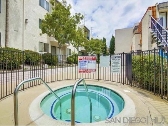 Outdoor jacuzzi area enclosed by a metal fence with adjacent multi-story residential buildings.