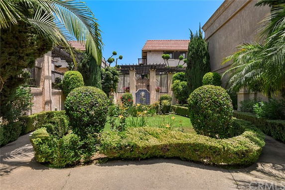 Front view of a building with decorative plants and hedges, and a red-tiled roof.