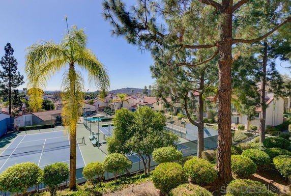 View of multiple tennis courts surrounded by residential buildings and lush trees.
