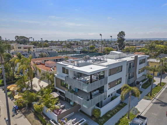 Aerial view of a modern three-story apartment building in a residential area with surrounding neighborhood houses.
