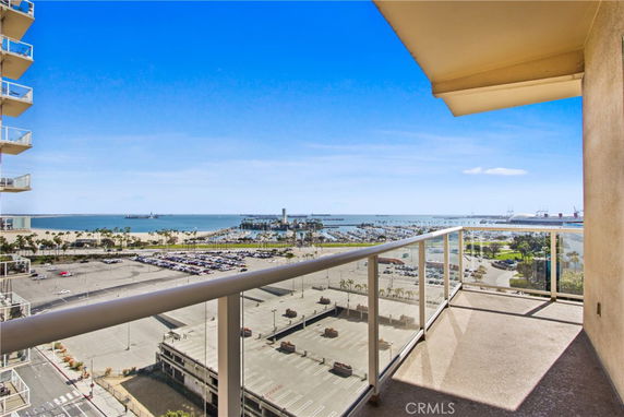 Balcony view overlooking a parking area with the ocean and distant ships in the background.