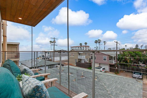 View from a balcony overlooking nearby houses and the ocean in the distance.